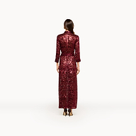 A woman stands facing away, wearing the maxi-length, long-sleeved Cameron Sequin Shirt Dress in red with black heels against a plain white background.
