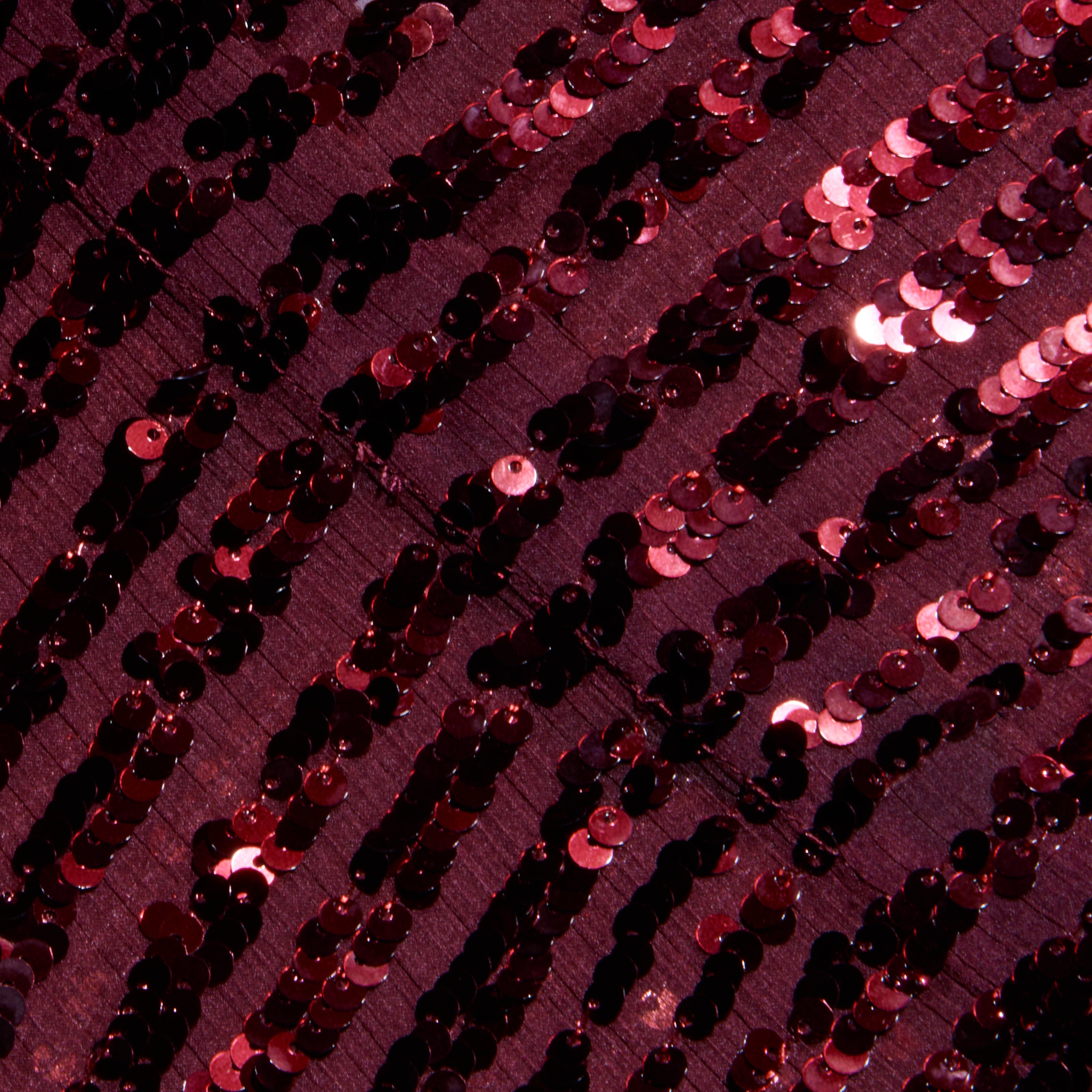 Close-up of the Cameron Sequin Shirt Dress, featuring dark red sequined stripes sewn in rows onto fabric. The sequins create a shiny, textured, and reflective surface that catches the light for a shimmering effect.