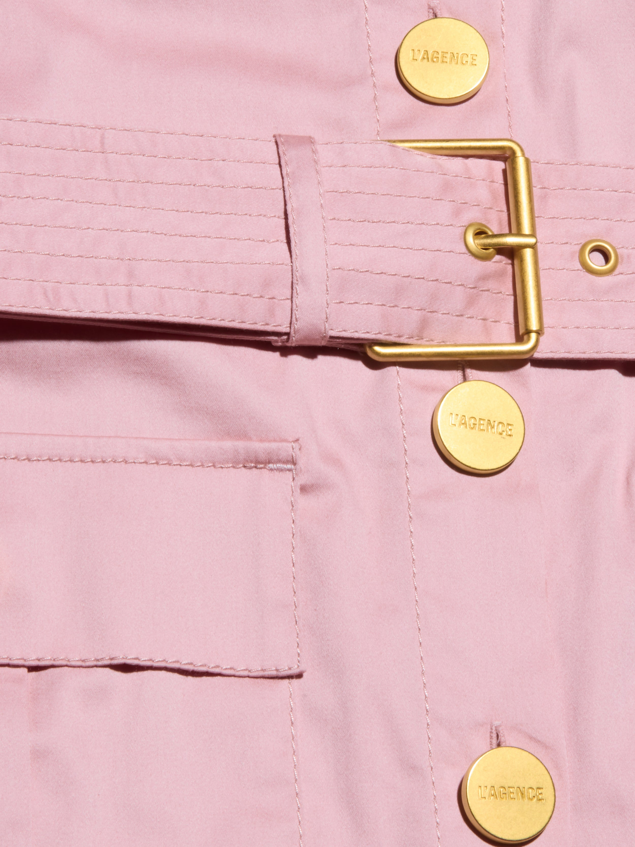 Close-up of the Noam Poplin Shirt Dress—a light pink utility jacket with a gold buckle belt, LAGENCE-stamped gold buttons, smooth fabric, and a front pocket.