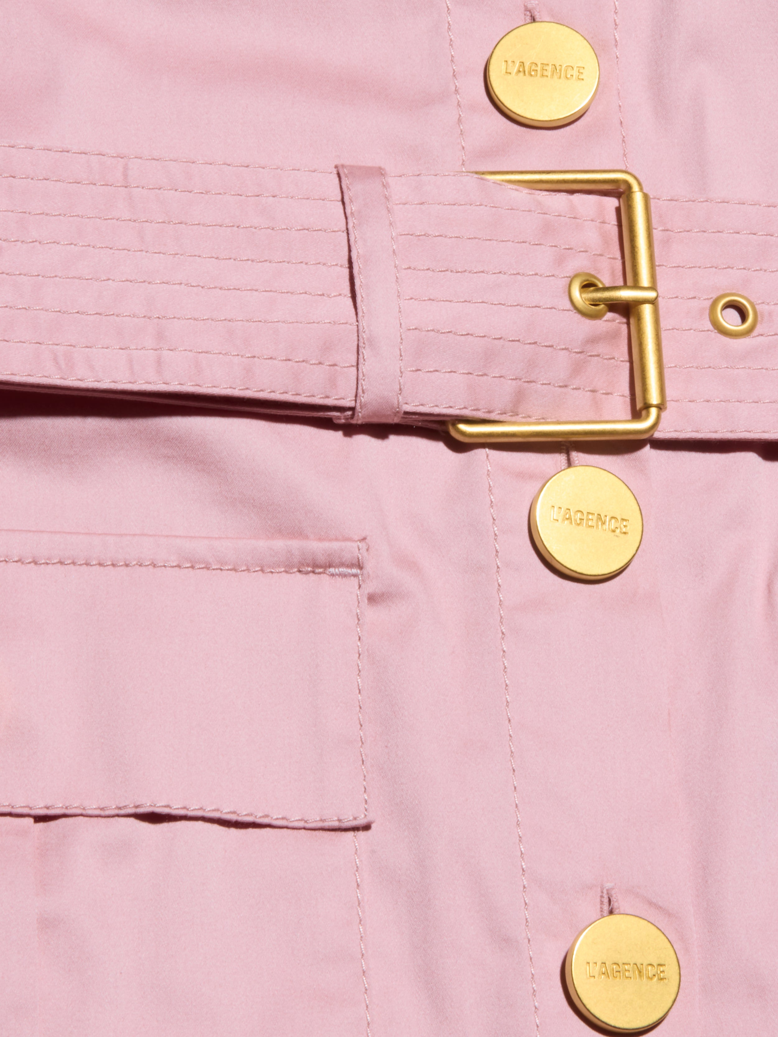 Close-up of the Noam Poplin Shirt Dress—a light pink utility jacket with a gold buckle belt, LAGENCE-stamped gold buttons, smooth fabric, and a front pocket.