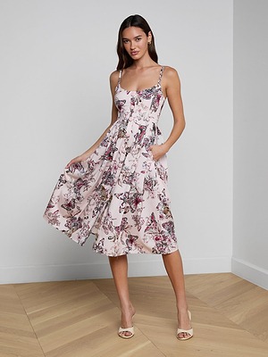 A woman poses indoors in the Reanne Midi Dress, a sleeveless linen midi with light pink butterfly jungle print and matching straps. She stands on a wooden floor, hand in pocket, wearing neutral heels for a playful look.