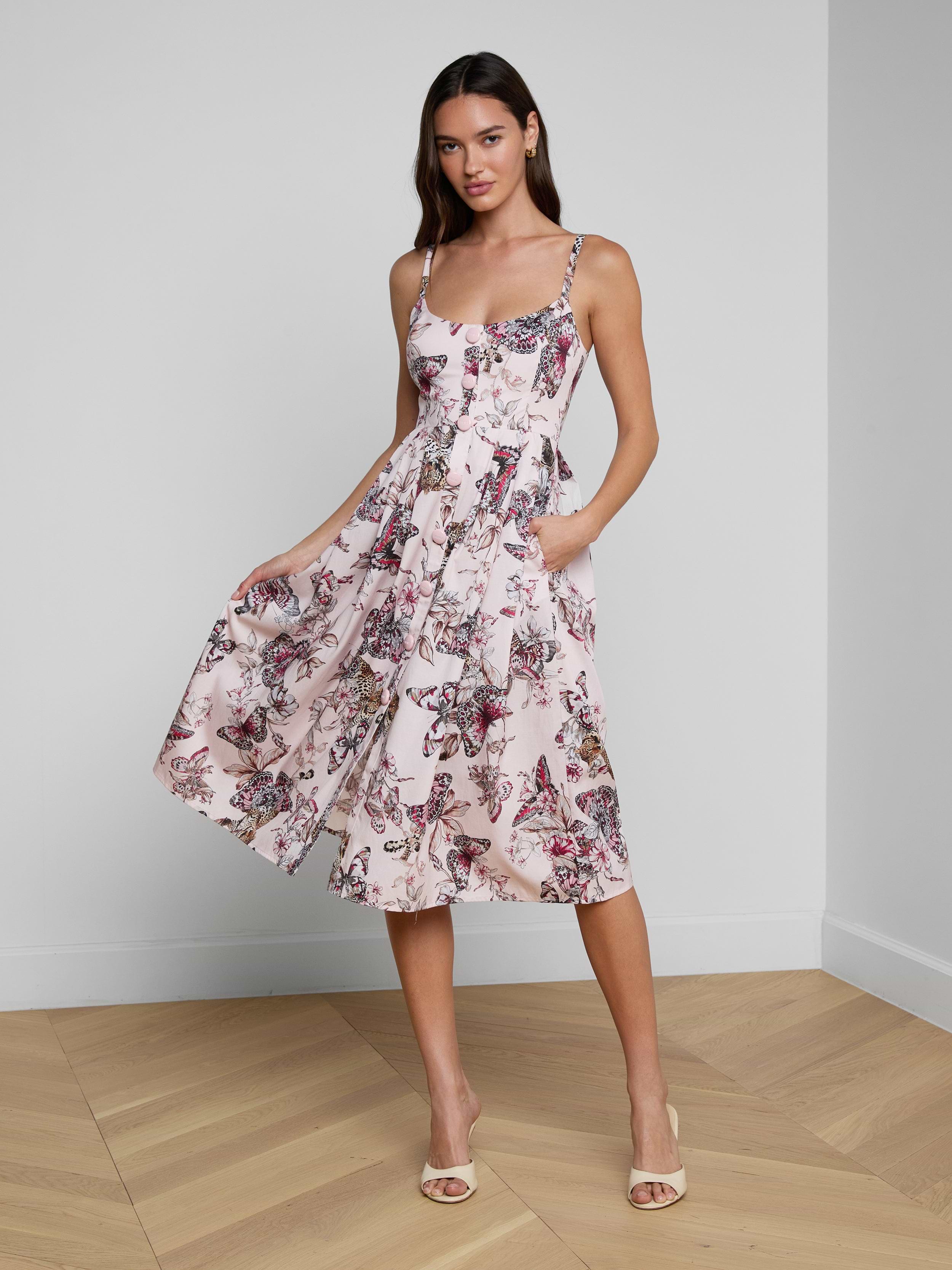 A woman wearing the Reanne Midi Dress—a sleeveless linen midi dress featuring a floral butterfly jungle print and spaghetti straps—holds the sides of the dress while standing against a plain white background.