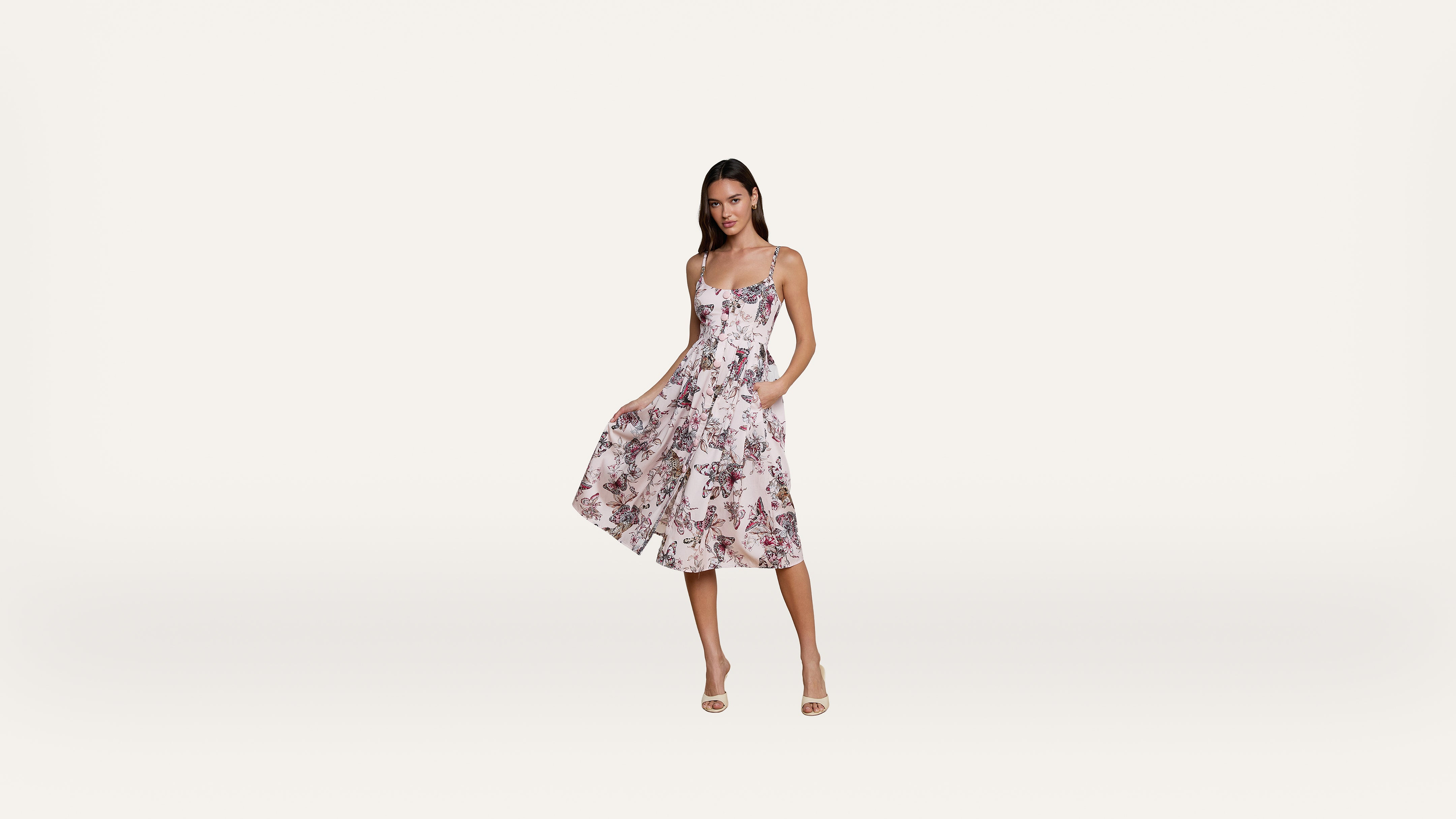 Woman wearing a sleeveless, floral print midi dress with a fitted bodice and flared skirt, standing in heels against a plain white background.