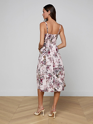 A woman stands facing away, wearing the Reanne Midi Dress—with a butterfly jungle print, thin straps, and midi length—paired with beige heels against a plain white background.