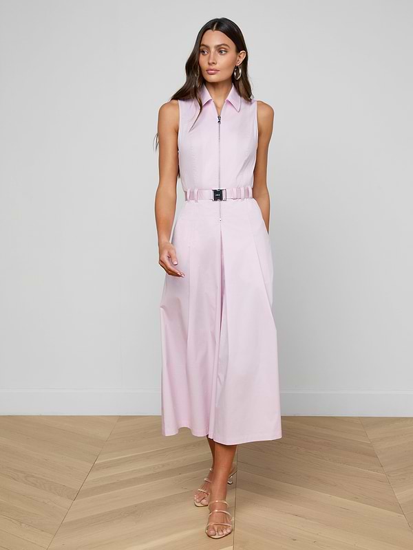 A woman wearing the Kolton Dress in sleeveless pastel lilac, styled with a statement belt and sandals, stands against a plain white background, gazing slightly to her right.