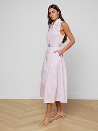 A woman stands against a white background wearing the Kolton Dress—a sleeveless, belted pastel lilac dress with pockets—paired with heeled sandals.