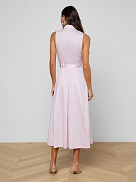 A woman stands with her back to the camera, modeling the sleeveless Kolton Dress in pastel lilac, accented with a statement belt and paired with beige heels against a plain white backdrop.