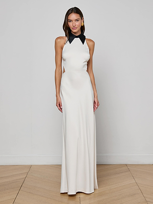 A woman poses on a wooden floor against a light gray wall, wearing the L'AGENCE Rossi Cutout Gown featuring a sleek design and contrasting black collar.