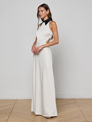 A woman poses on a wooden floor against a light-gray background, wearing the L'AGENCE Rossi Cutout Gown—a sleek maxi dress with side cutouts and a contrasting black collar.
