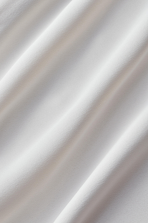 Close-up of smooth, white fabric with gentle folds and soft shadows, capturing the elegant flowing texture of the Rossi Cutout Gown by L'AGENCE.