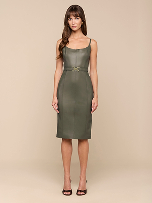 تقف امرأة على خلفية باللون البيج، ووجهها إلى الأمام، وهي ترتدي فستان Halia Vegan Leather Dress باللون الزيتوني الدخاني - وهو فستان متوسط الطول بلا أكمام مع حزام خصر - مع صندل أسود بكعب عالٍ.