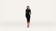 A woman with long hair wearing a fitted black dress and black heels stands against a plain white background, looking at the camera with a neutral expression.