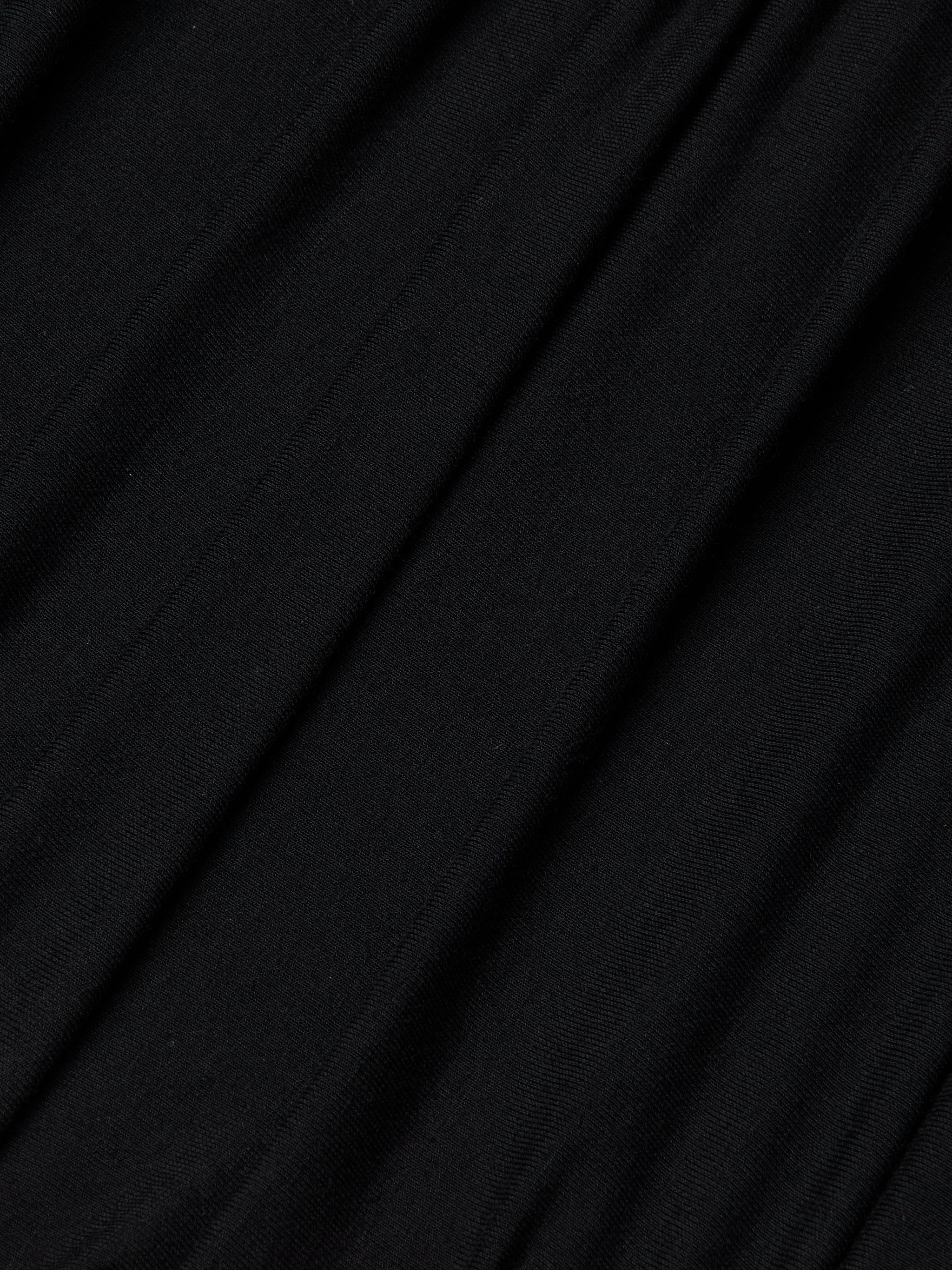 Close-up of the Paityn Shirred Dress’s smooth, black stretch jersey fabric with gentle folds and soft texture, creating subtle diagonal lines and shadows across the surface.