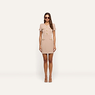 A woman wearing a tan Cori Mini Dress with gold-tone hardware and two front pockets, paired with sunglasses and open-toe heels.