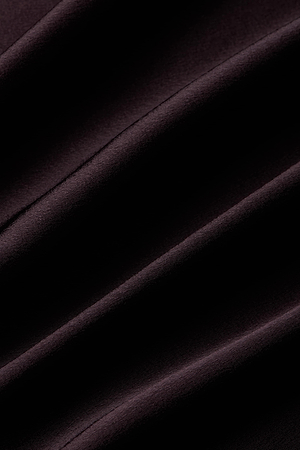 The L’AGENCE Manon Satin Gown features soft, dark fabric with subtle diagonal folds that create elegant shadows and highlights, offering a refined and sophisticated texture.