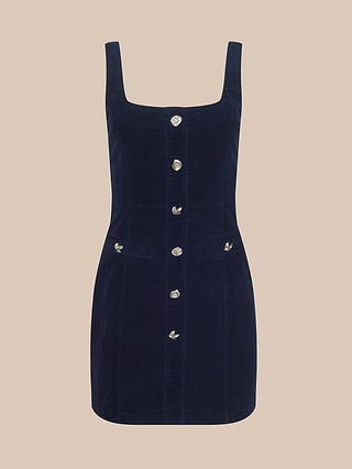 The Vynna Corduroy Dress is a navy blue, sleeveless mini dress crafted from stretch corduroy. It features a flattering A-line silhouette with a square neckline, silver buttons down the front, and two small front pockets, displayed on a beige background.