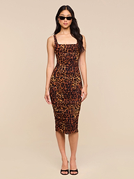 A woman stands facing forward with her arms relaxed at her sides, wearing the Anya Shirred Dress—a form-fitting leopard print midi dress—paired with black sunglasses and black open-toe heels. The background is plain white.