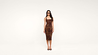 Woman wearing sunglasses and a fitted, sleeveless, knee-length leopard print dress with black high-heeled sandals, standing against a plain white background.