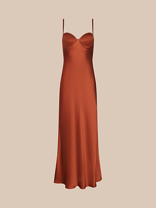 La robe « Sayla Silk Gown », une robe nuisette sans manches de couleur orange brûlé, confectionnée dans un satin somptueux, dotée de fines bretelles et dun corsage ajusté, évoque le glamour vintage et est présentée sur un fond beige uni.