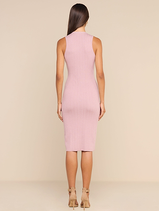 A woman with long brown hair is standing with her back to the camera, wearing the Domino Dress—a form-fitting, sleeveless midi dress in a light pink shade—paired with beige heels against a plain beige background.