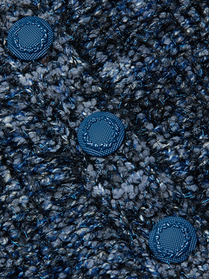 Close-up of the Una Knit Cardigan by L'AGENCE shows textured, woven blue and black fabric with three round, textured blue buttons arranged diagonally across the surface.