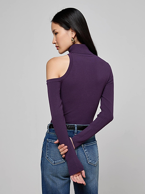 A woman with long dark hair models the L'AGENCE Azia Cutout Knit Top in purple, paired with blue jeans, standing with her back to the camera and her hands crossed behind her.