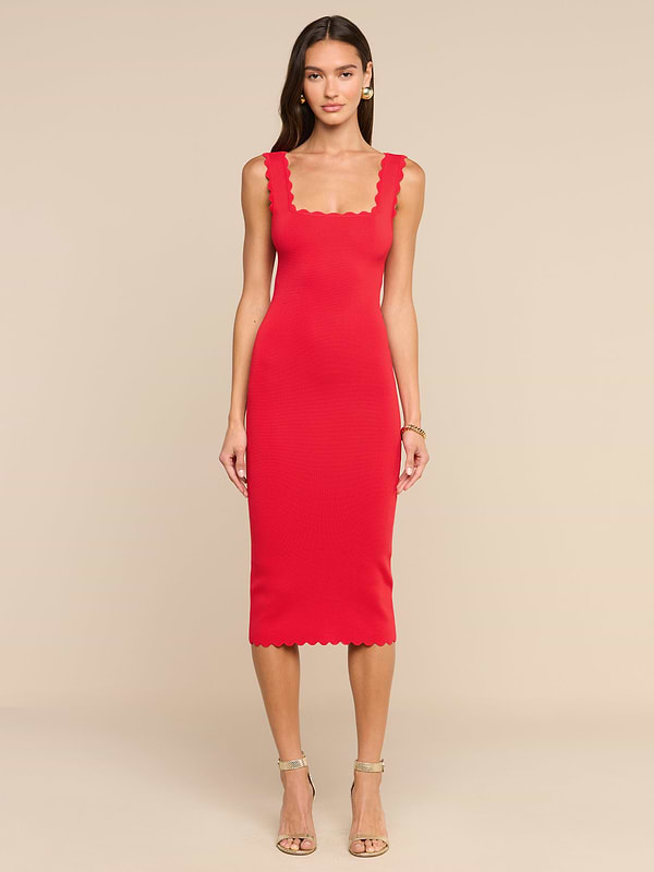 Una donna è in posa su uno sfondo beige e indossa l’abito in maglia Romona: un miniabito senza maniche, dalla linea aderente, di colore rosso rossetto, caratterizzato da scollo quadrato smerlato e orlo smerlato. Ha i capelli lunghi e abbina il look a sandali beige con tacco alto e cinturini e a un braccialetto.