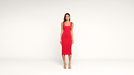 A woman stands against a plain white background wearing a fitted, sleeveless red dress with a square neckline and scalloped edges, paired with strappy high-heeled sandals.