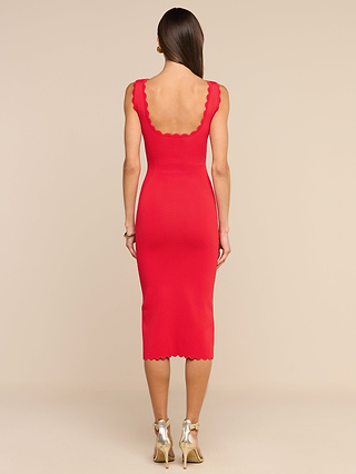 A woman stands with her back to the camera, wearing a fitted, sleeveless, knee-length Romona Knit Dress in lipstick red with scalloped edges and gold high-heeled sandals, set against a plain beige background.