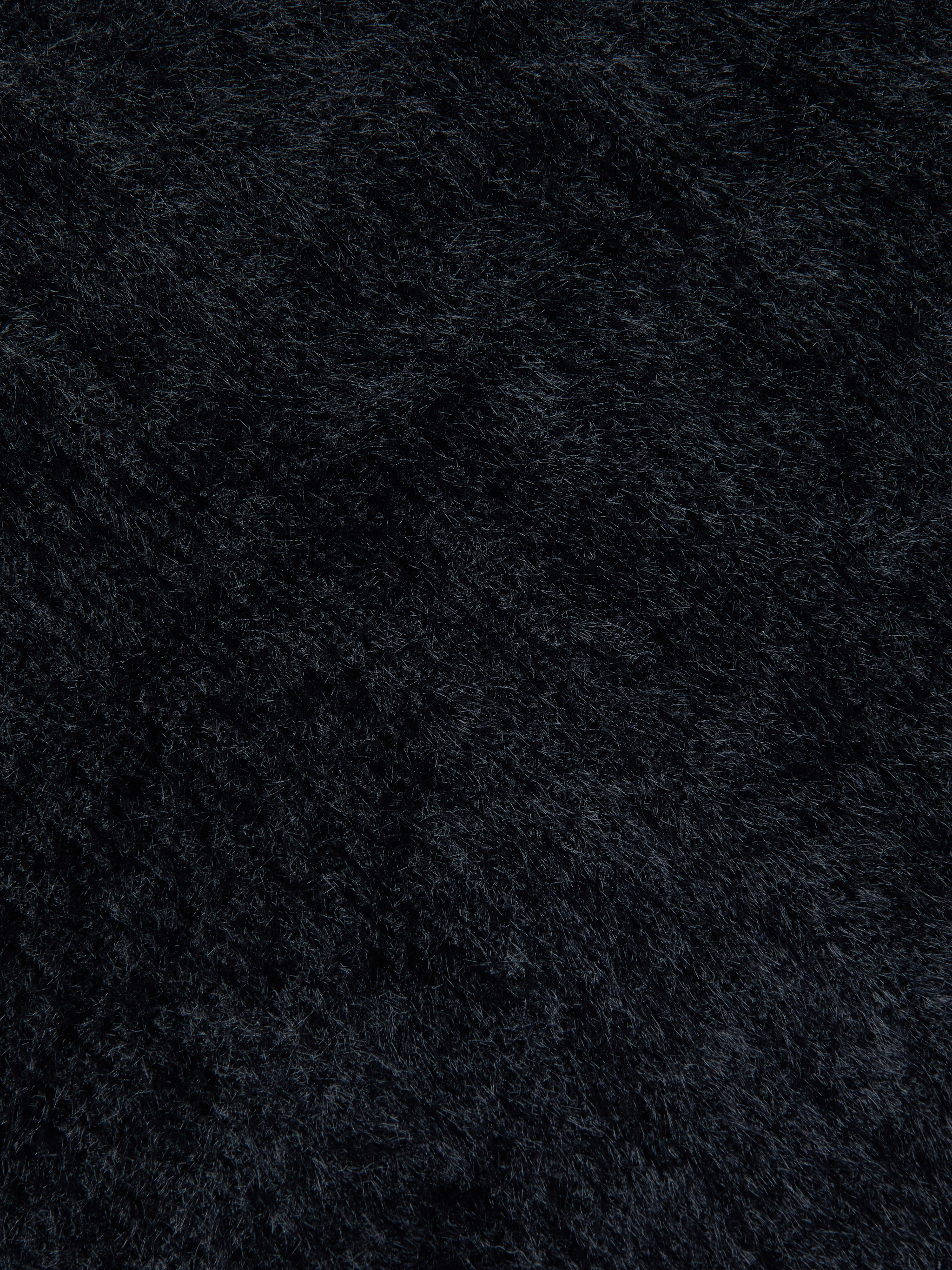 Close-up of the ultra-soft knit fabric of the Guinevere Cropped Pullover in black, highlighting the plush surface, fine fiber details, and subtle directional variations.