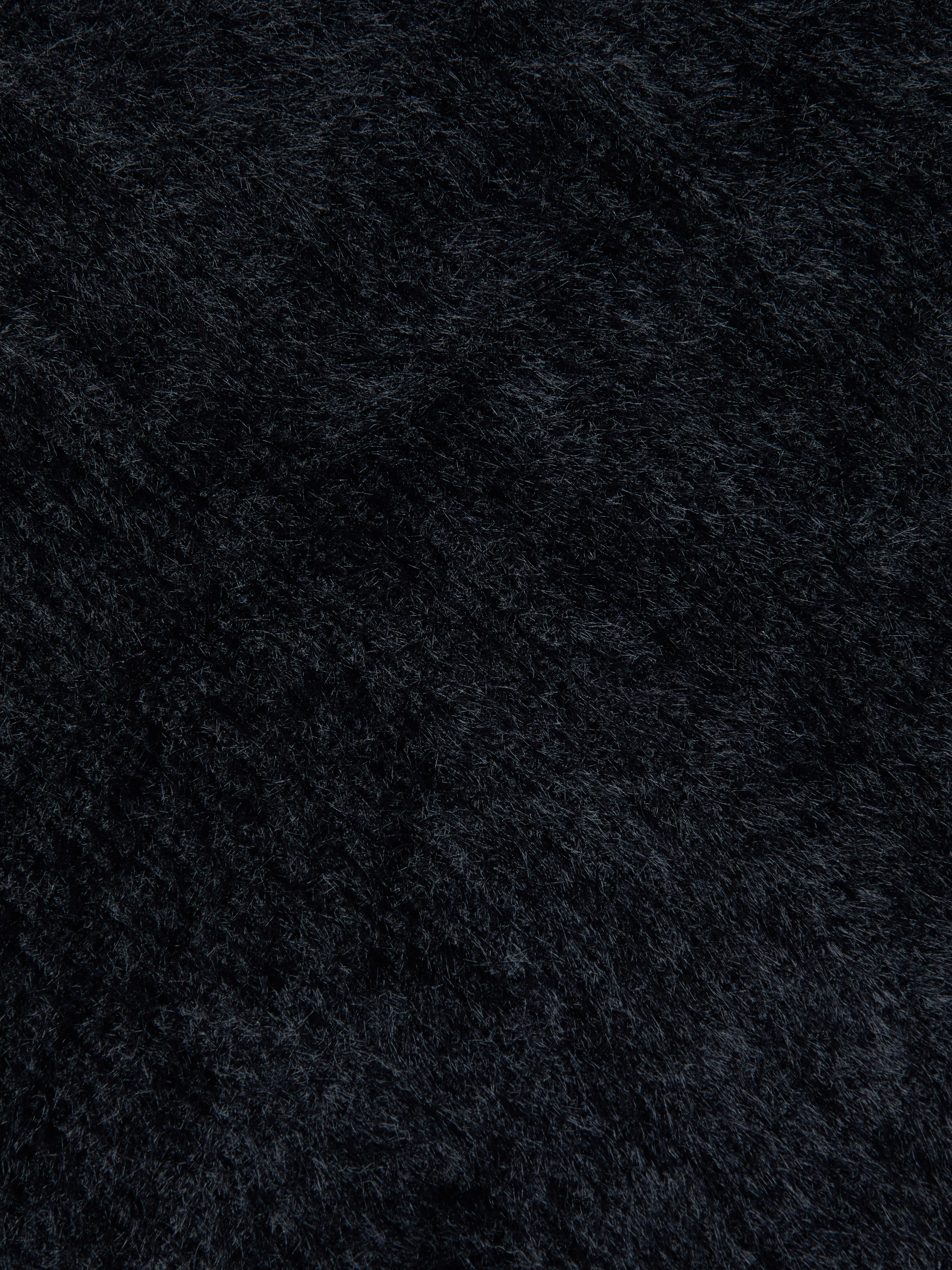 Close-up of the ultra-soft knit fabric of the Guinevere Cropped Pullover in black, highlighting the plush surface, fine fiber details, and subtle directional variations.