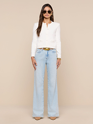 Woman in the Patsy Cropped Cardigan—a white long-sleeve top with ribbed trims—paired with light blue wide-leg jeans, tan heels, and sunglasses stands against a plain white background. She has long hair down and accessorizes with a belt and bracelets.
