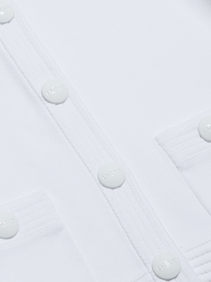 Close-up of the Patsy Cropped Cardigan in ivory, showcasing white embossed buttons, two front pockets, visible stitching, and smooth structured fabric with refined ribbed trims for a polished finish.