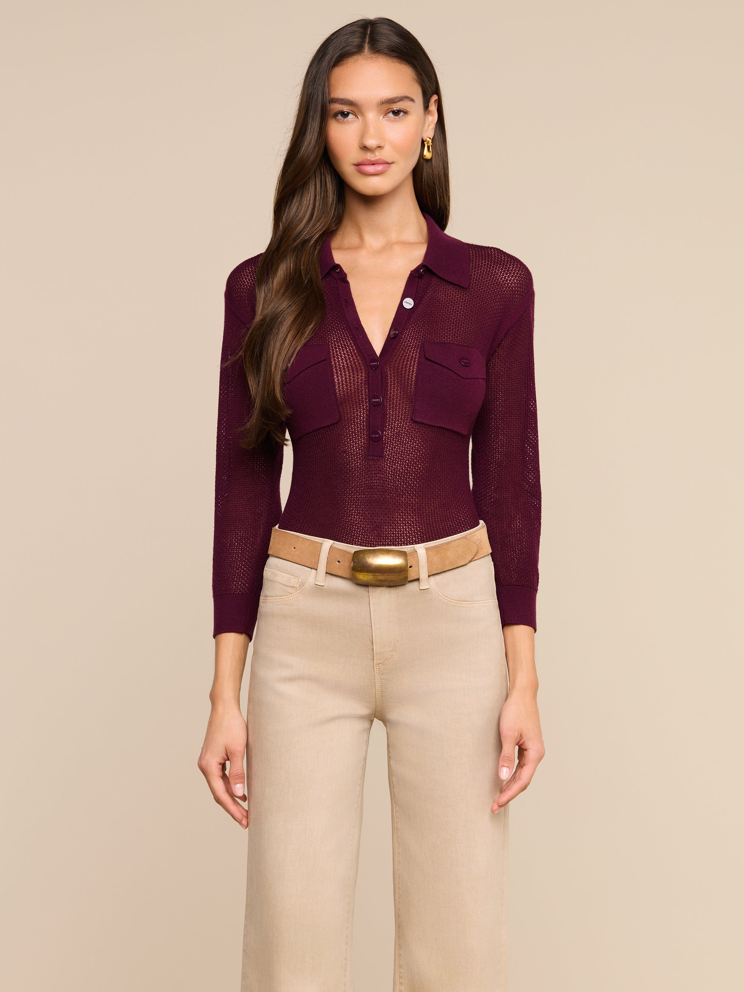 A woman wearing a burgundy Carine Top with utility pockets and beige wide-leg pants with a large belt stands facing forward against a plain light background.