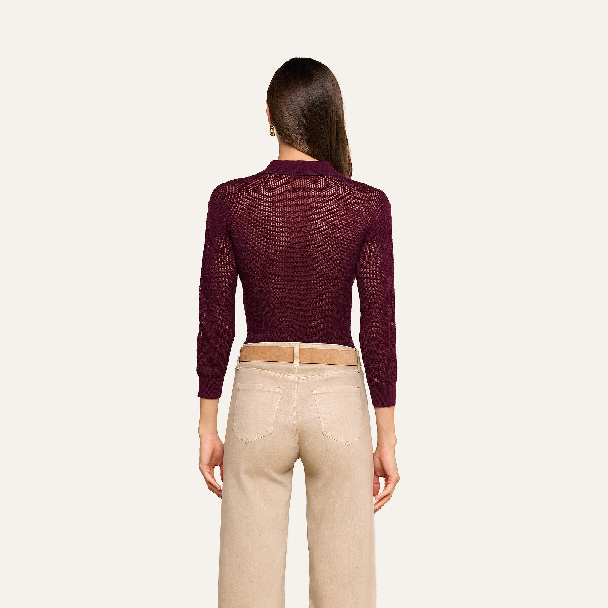 A woman stands facing away, wearing a maroon Carine Top and high-waisted beige pants. Her straight brown hair is down, and she is against a plain, light background.