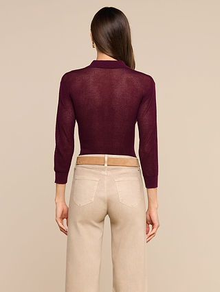 A woman faces away, wearing a maroon Carine Top crafted from lightweight knit and high-waisted beige pants with belt loops, set against a plain beige background.