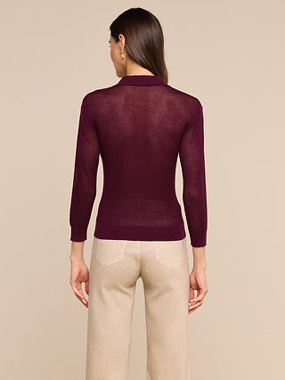 A person stands facing away against a plain beige background, wearing the Carine Top—a sheer, lightweight knit, long-sleeve dark burgundy top—paired with light beige utility pocket pants.