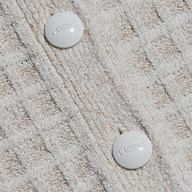 Close-up of cream bouclé yarn fabric with a grid pattern on the Novalie Cardigan Top, featuring two round white buttons embossed with the word LAGENCE.