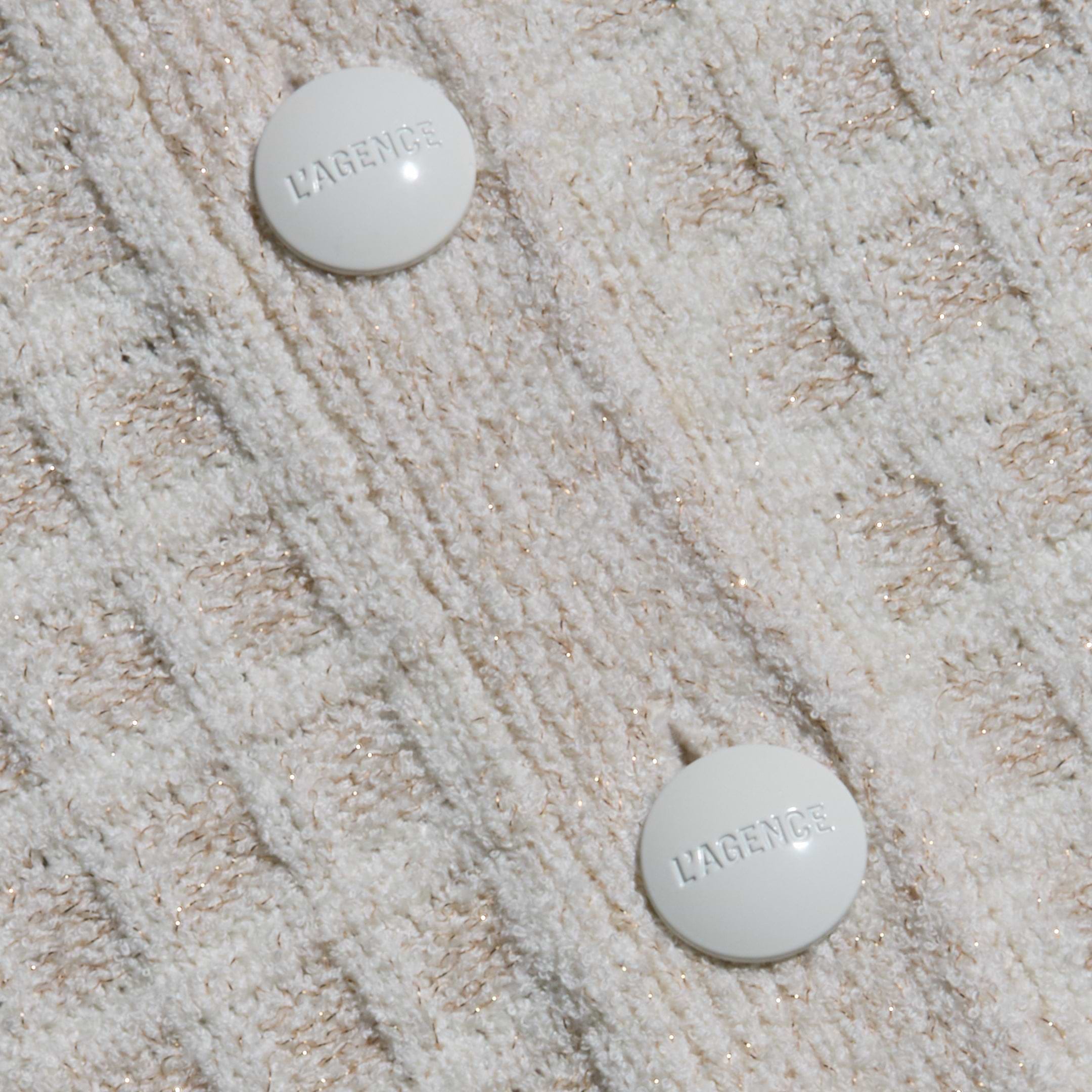 Close-up of cream bouclé yarn fabric with a grid pattern on the Novalie Cardigan Top, featuring two round white buttons embossed with the word LAGENCE.