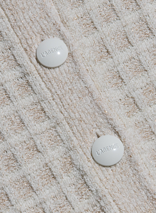 Close-up of the Novalie Cardigan Top’s cream and gold knit fabric, featuring a bouclé yarn tweed texture and two white round buttons embossed with “L’AGENCE.”.