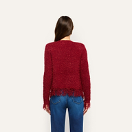 Back view of a person wearing a bold, textured red Mireille Fringe Cardigan with fringed hems, paired with blue jeans.