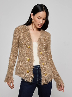 A woman models the Azure Fringe Cardigan Blazer by L’AGENCE, featuring a textured beige knit with large gold buttons, worn over a cream top and dark jeans against a plain light gray background.