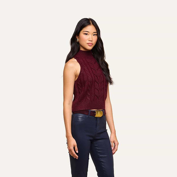 A woman stands against a plain background wearing the Bellini Cable-Knit Top and navy blue pants with a brown belt.