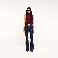 A woman stands against a plain white background, wearing sunglasses, the Bellini Cable-Knit Top in merlot red, dark blue flared pants with a belt, and maroon pointed-toe shoes.