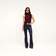 Woman wearing sunglasses, a Bellini Cable-Knit Top in merlot red, navy flared pants, and burgundy shoes stands confidently against a plain white background.