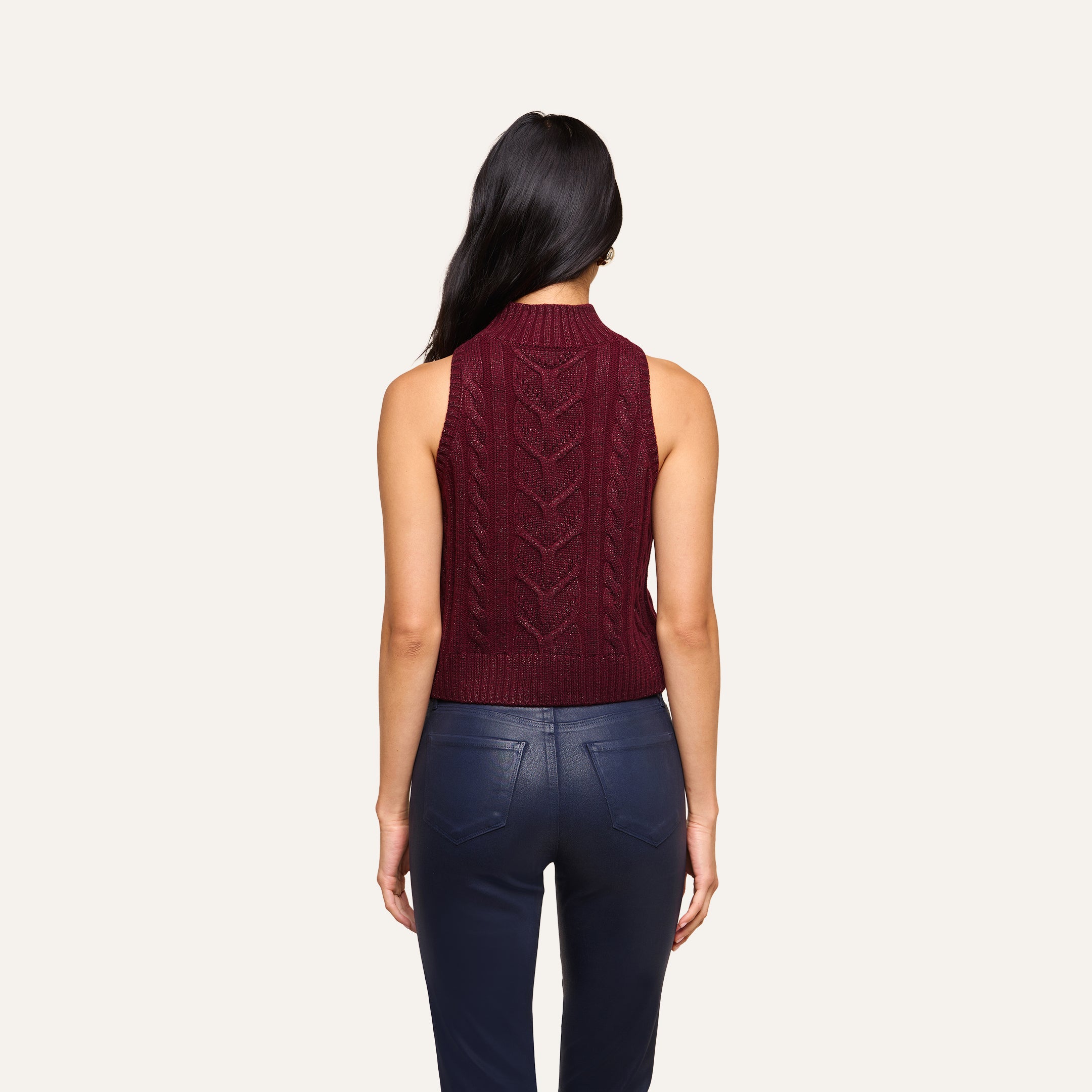 A woman with long dark hair, seen from behind, wears the Bellini Cable-Knit Top in merlot red and dark blue pants against a plain light background.
