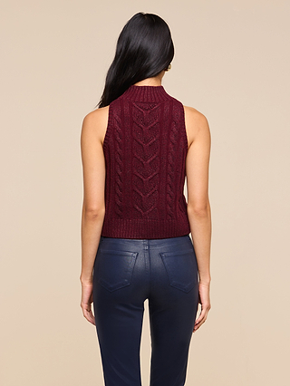 A woman with long dark hair wears the Bellini Cable-Knit Top— a sleeveless maroon sweater—paired with dark blue pants, shown from the back against a plain beige background.