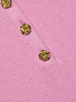 Close-up of the Sterling Sweater, featuring pink textured knit fabric and a row of shiny gold floral buttons along a diagonal seam—an elegant detail on this slim fit henley top.