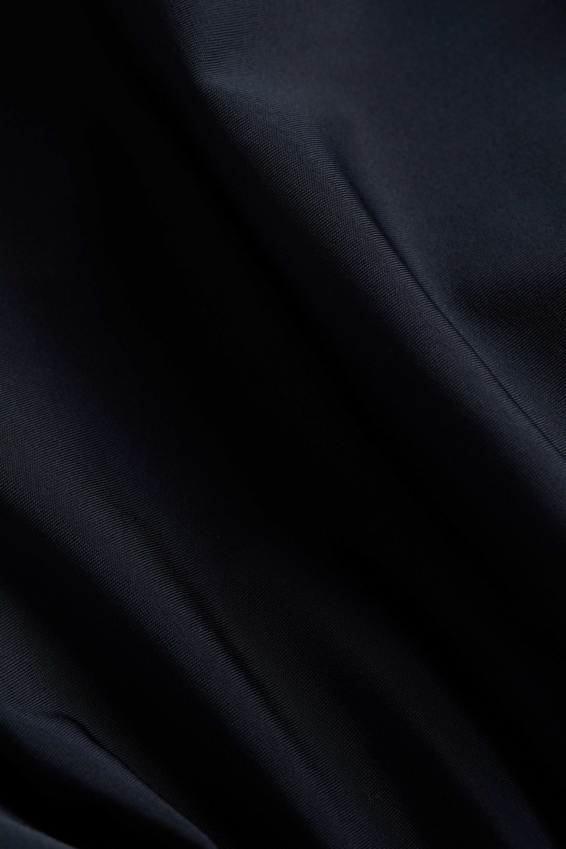 Close-up of smooth, dark navy blue fabric with soft folds and gentle light reflections highlighting the texture, reminiscent of the versatile Nicole Bikini Bottom.