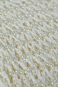 Close-up of the Angela Crochet Cover-Up Dress, featuring a white crocheted fabric with an open, lacy pattern, decorated with evenly spaced small, shiny faux pearl accents throughout the design.